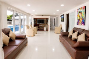 Ampla sala de estar com vista para a piscina, sofás de couro e uma televisão.