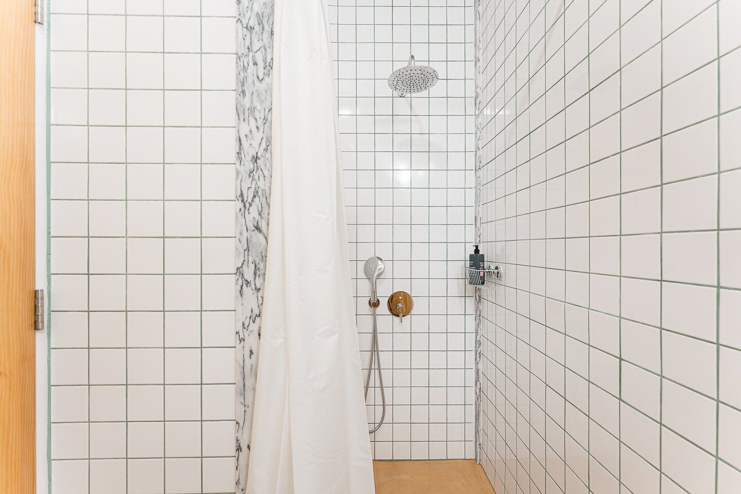 Ein geflieseltes Badezimmer mit Dusche, Handtuchhalter und Seifenspender.