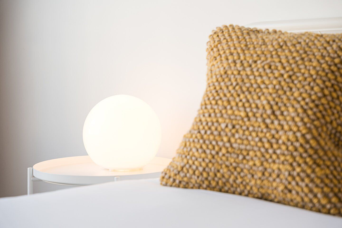 A round light fixture on a white surface with a textured pillow beside it.