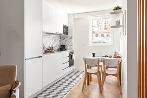 A compact kitchen with white cabinetry, a marble backsplash, and a dining area with a small table and chairs. - GuestReady - Fantastic Porto Flat (Porto)