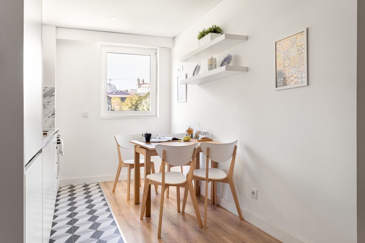 A small kitchen with a dining table and chairs, a window with a city view, and a patterned floor.