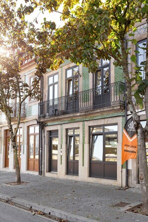 Edifício com espaço comercial no térreo e unidades residenciais nos andares superiores, com varanda e grades de metal.