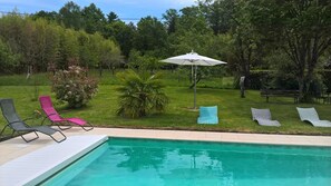 Ein Swimmingpool mit Liegestühlen und einem Sonnenschirm, umgeben von einer Rasenfläche und Bäumen.