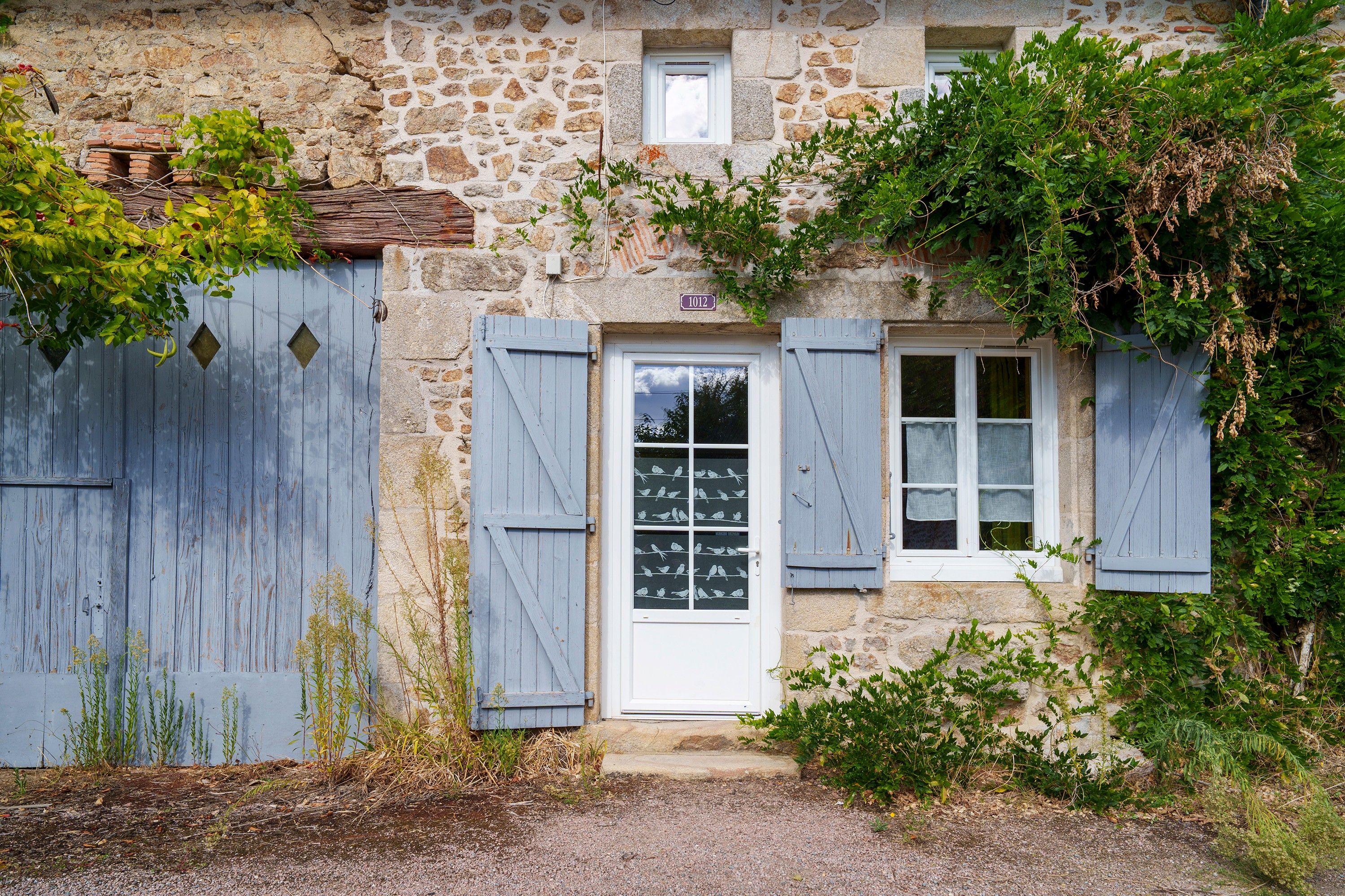 Ein Steinhaus mit einer Holztür und -läden, einem kleinen Fenster und einem Hausnummernschild.