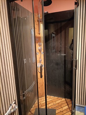 Ein Duschbereich mit Glastür, Holzverkleidung und einer Duschbrause.