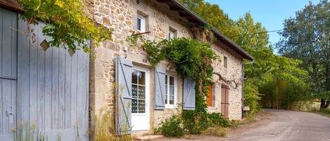A stone building with a gravel driveway, wooden shutters, and a clear sky.