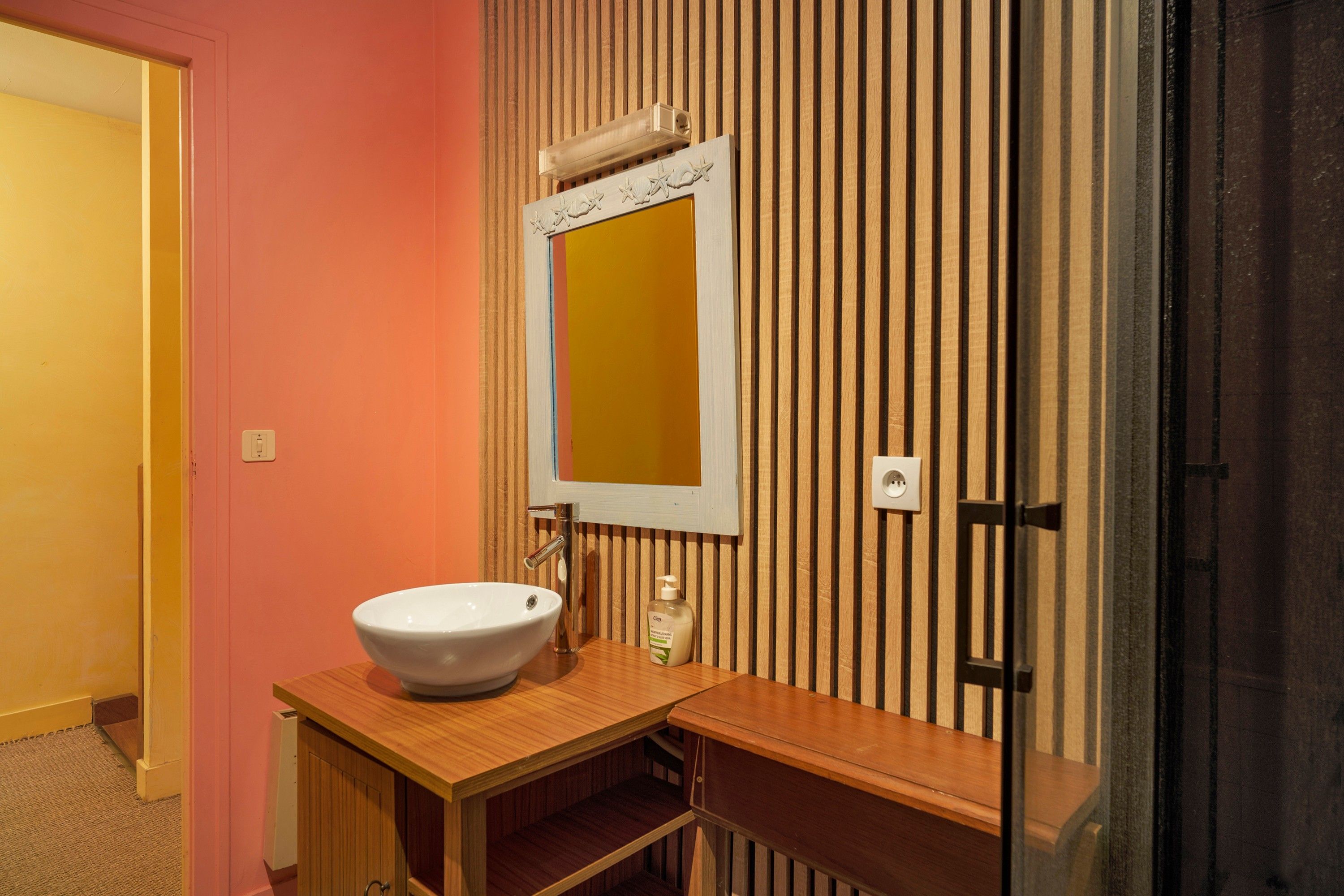 Une salle de bain avec un lavabo blanc, un miroir et un meuble-lavabo en bois.