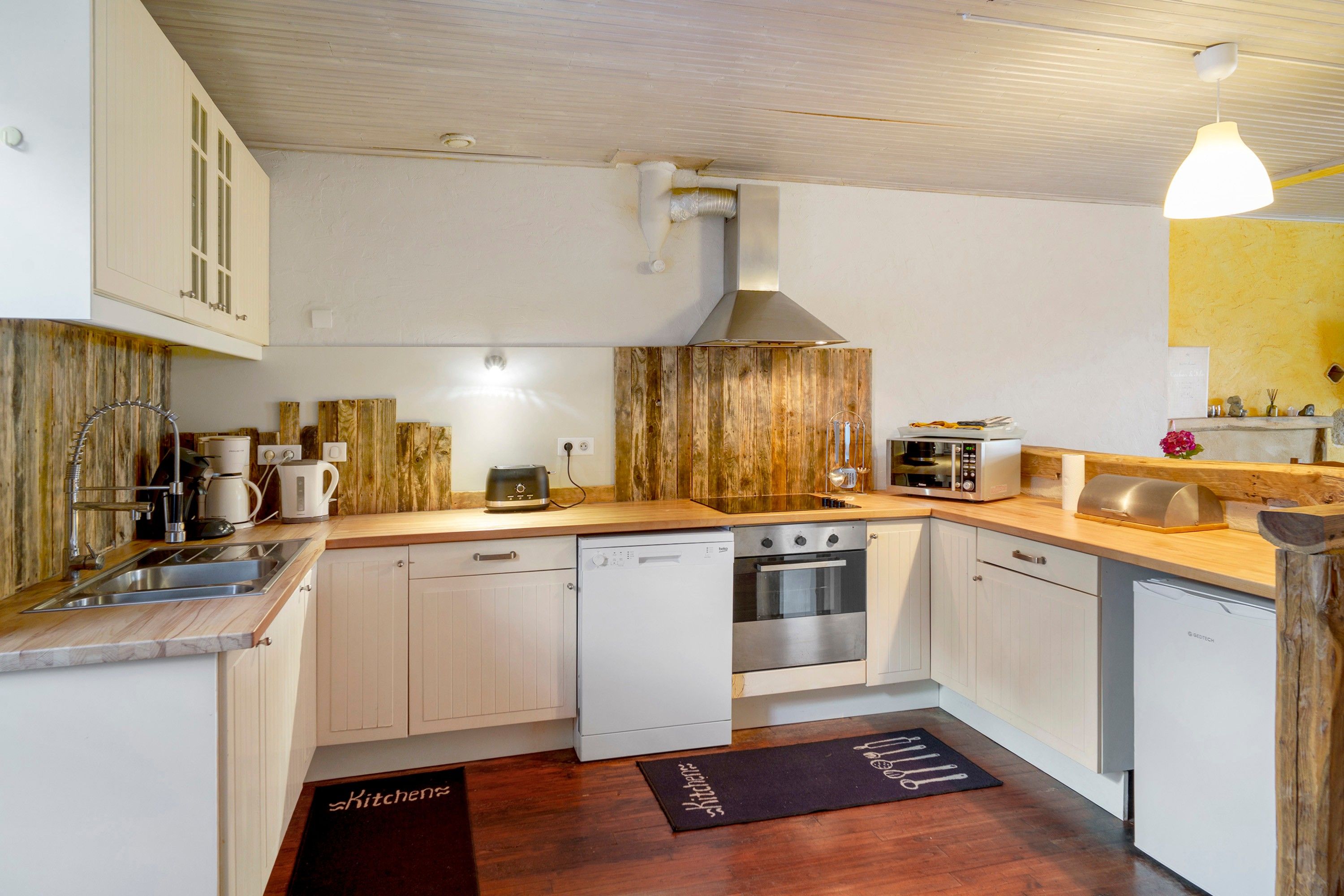 Eine kompakte Küche mit weißen Schränken, einer Holz-Akzentwand, einem Einbauofen und einer Kaffeemaschine.