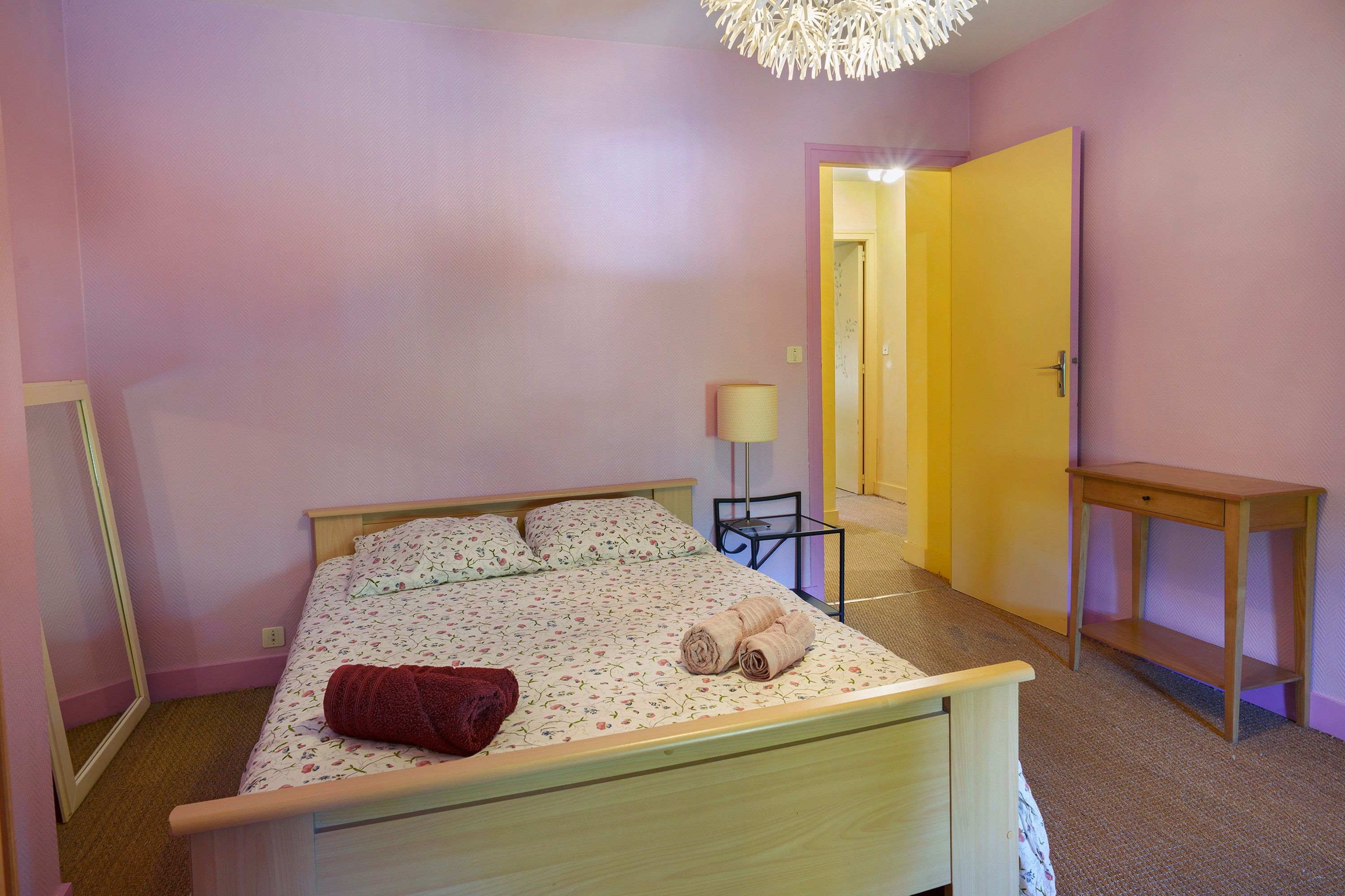 Ein Schlafzimmer mit einem Bett, einem Nachttisch, einer Lampe und einer Tür zu einem anderen Raum.