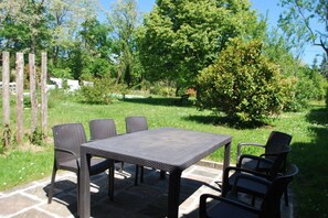 Eine Terrasse im Freien mit Tisch und Stühlen, umgeben von Grünpflanzen und Bäumen.