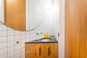 A bathroom with white tiled walls, a wooden vanity with a sink, and a mirror. - GuestReady - House of Many Faces - Room 3 (Porto)
