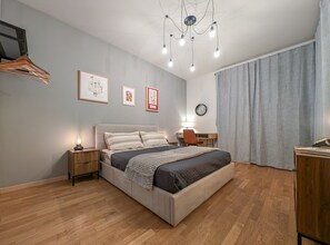 Una camera da letto con un letto, comodini, una scrivania, una sedia, una lampada a sospensione e una finestra con tende.