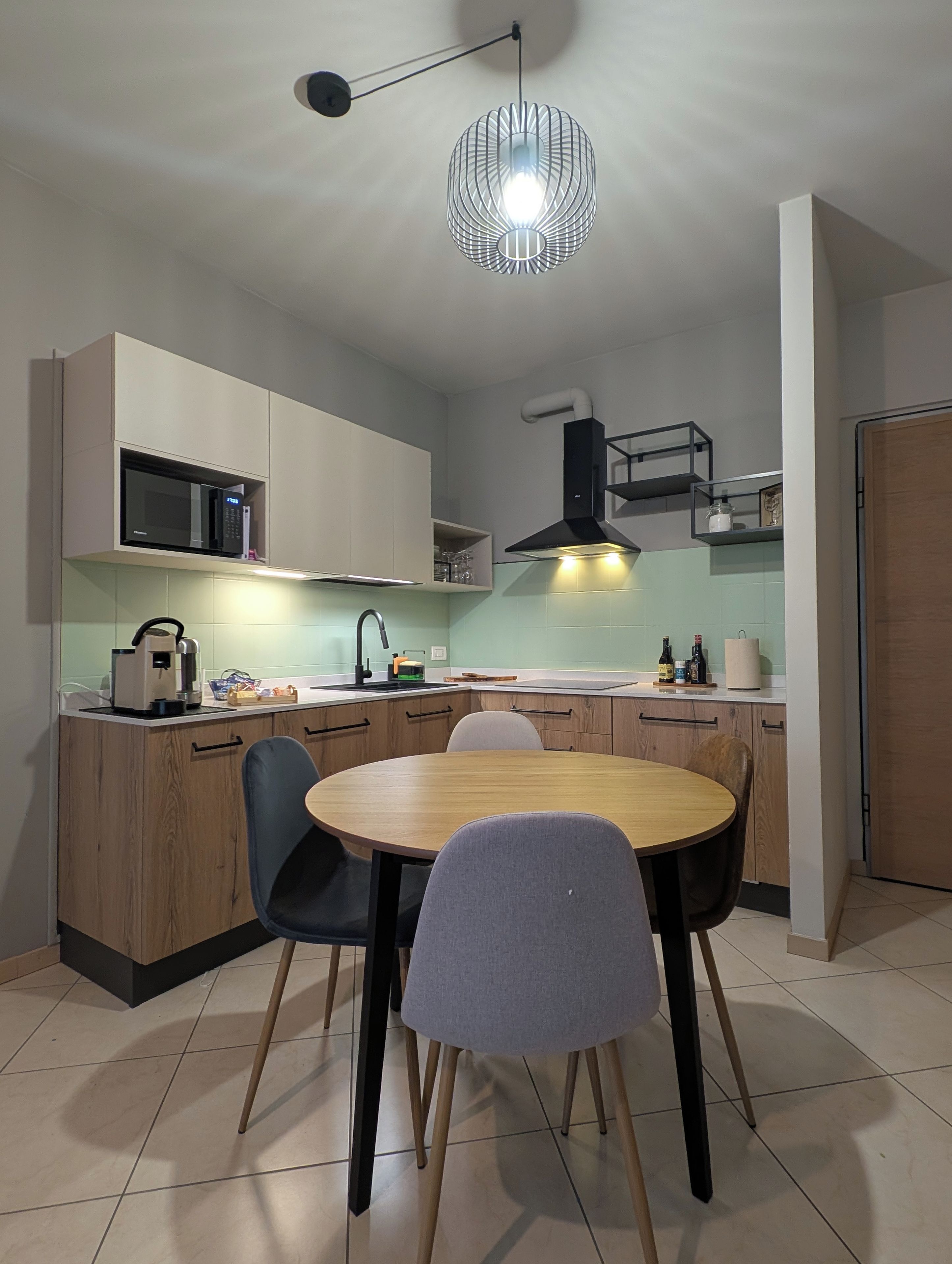 Una cucina moderna con un tavolo da pranzo rotondo, elettrodomestici integrati e una lampada a sospensione.