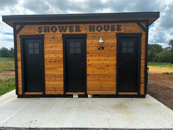 A wooden structure labeled 'SHOWER HOUSE' with three black doors and a small light fixture above the center door.