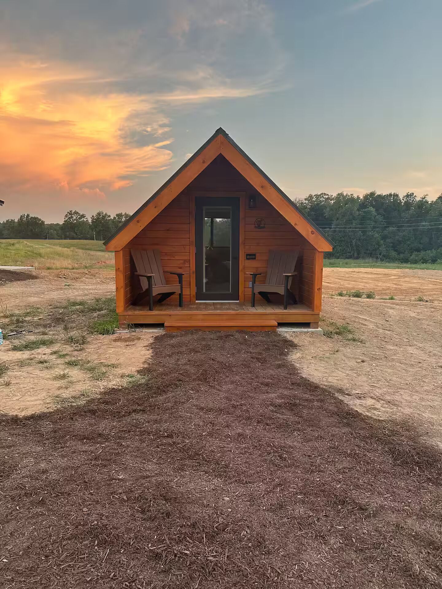 Una cabaña de madera con un porche, dos sillas y una puerta.