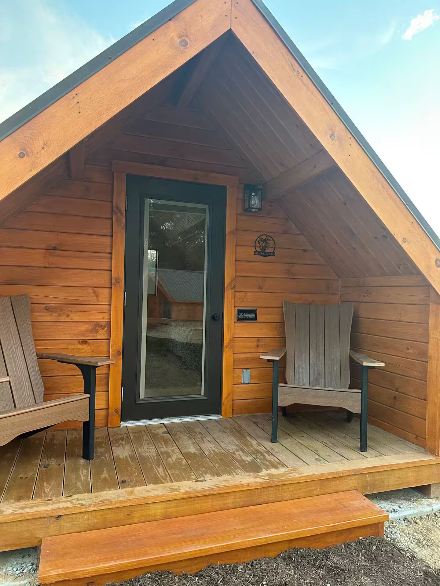 Una cabaña de madera con techo inclinado, una puerta principal y dos bancos en el porche.