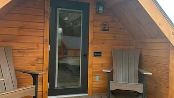 Una cabaña de madera con techo inclinado, una puerta principal y dos bancos en el porche.