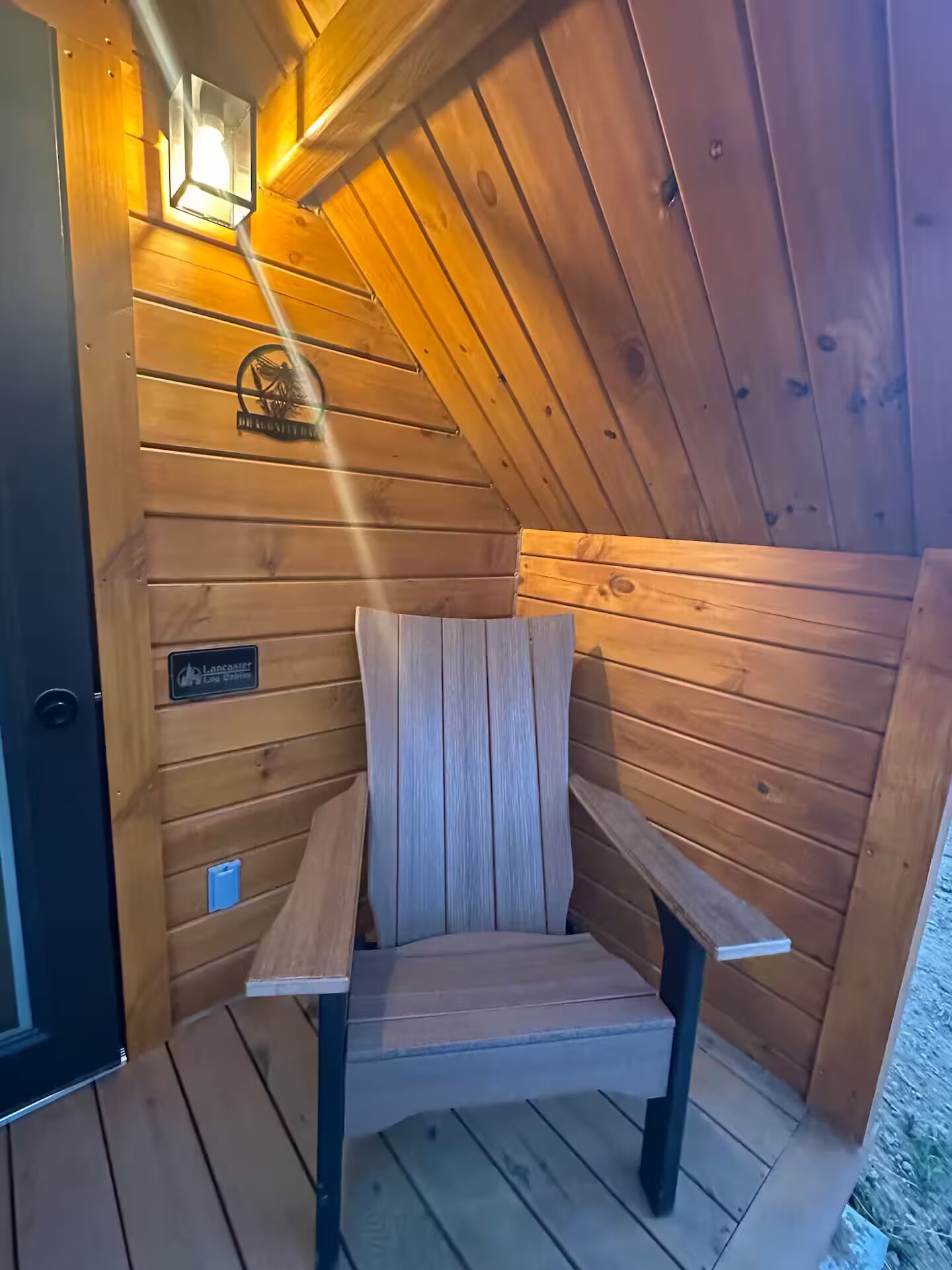 Una cabaña de madera con un banco, un letrero que dice 'Lancaster Long Cabins' y una puerta.