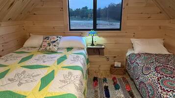 Un dormitorio acogedor en el ático, con dos camas, una ventana y una mesita.