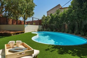 A swimming pool with artificial grass, a wooden deck, and a table with cups and a book. - Ca la Calma, Palau-Saverdera (Palau-saverdera)