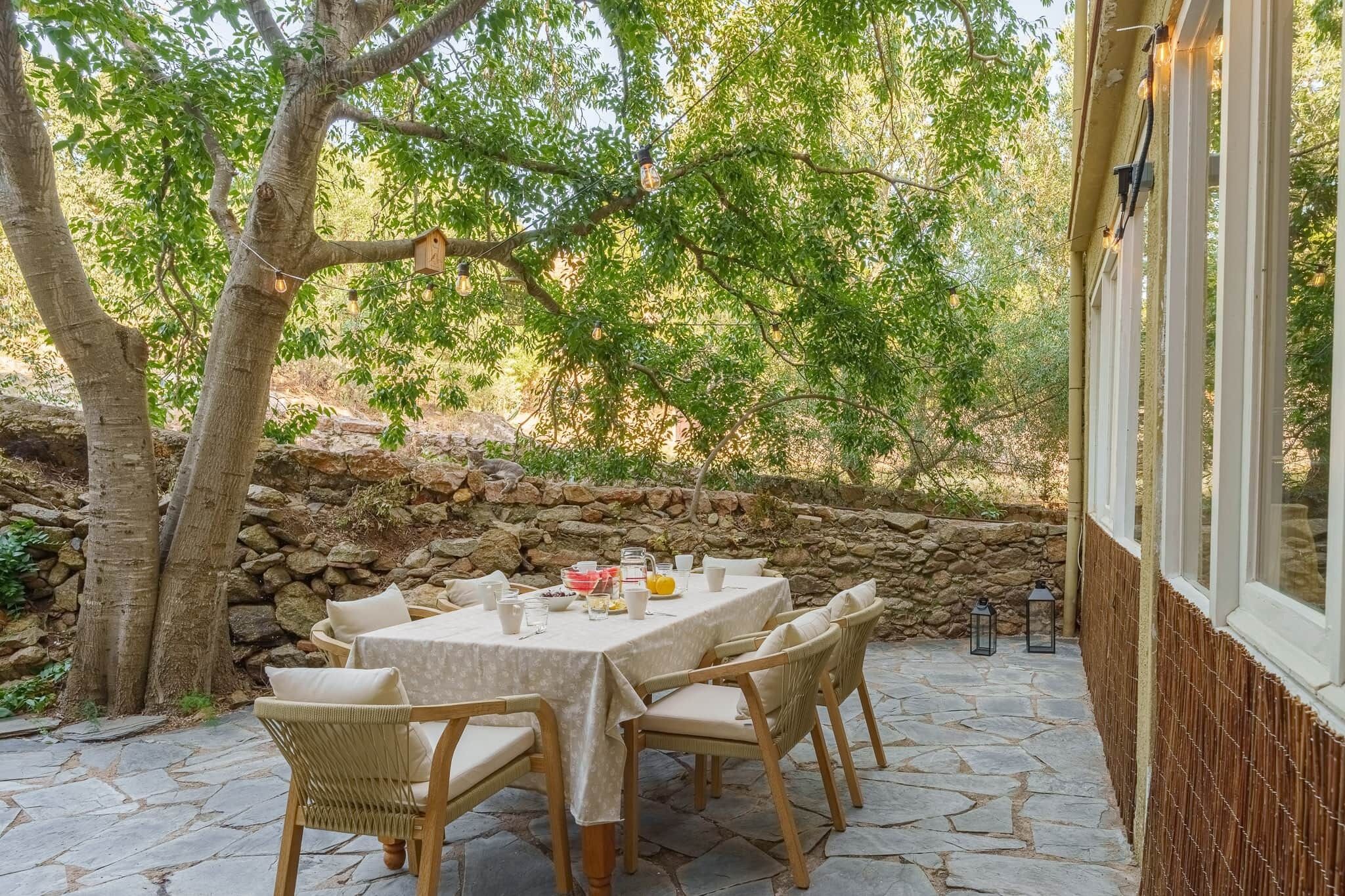An outdoor dining area with a stone wall, a wooden table, and wicker chairs.
