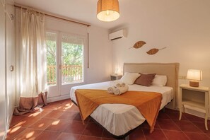 Hotellihuone, jossa on sänky, yöpöytä, lamppu, ikkuna verhoilla ja ilmastointilaite.