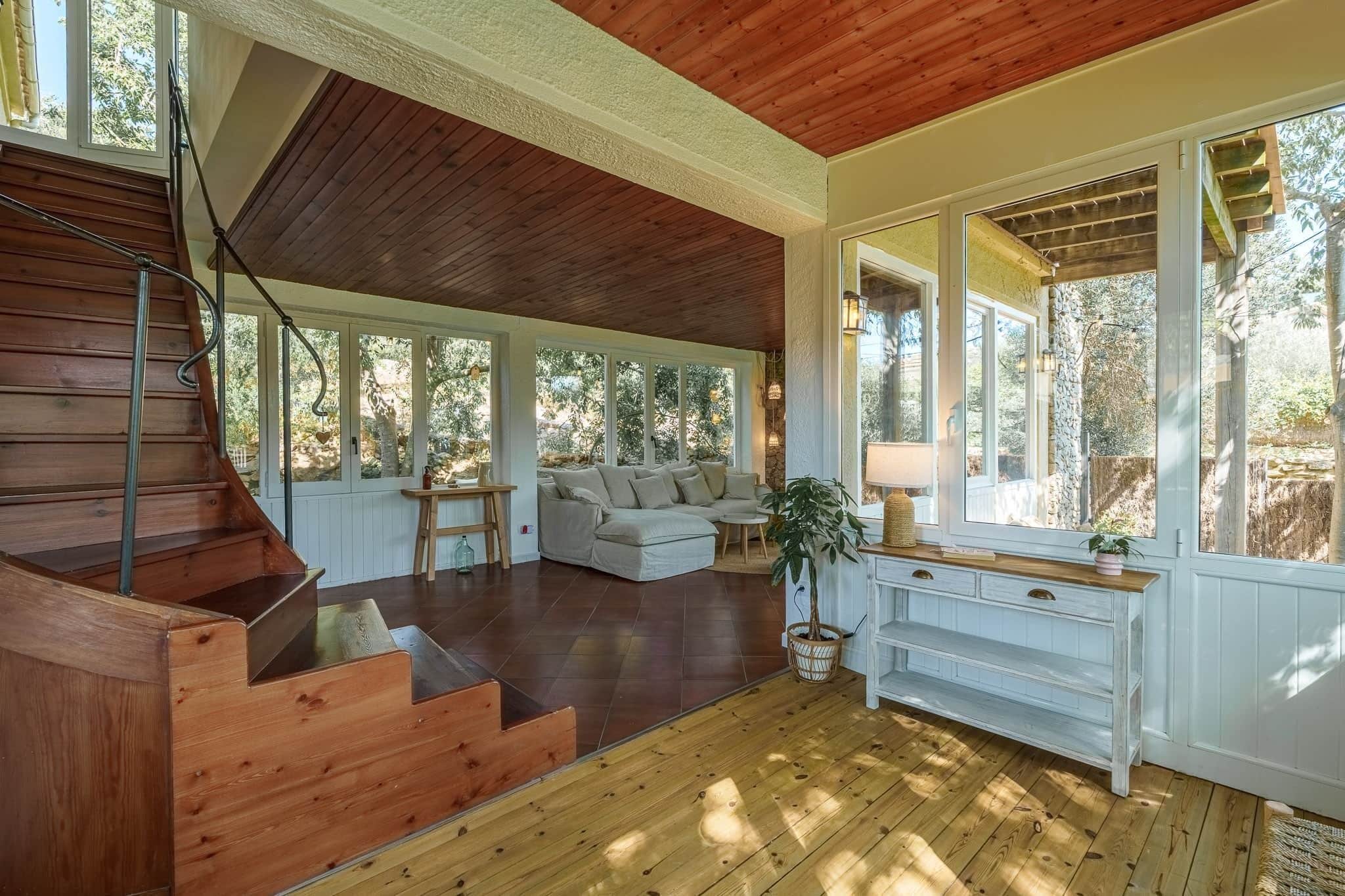 A spacious living area with a wooden staircase, a sofa set, and a dining table.