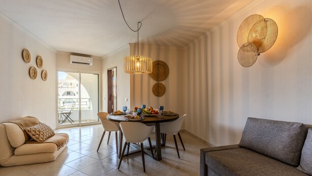 A modern living room with a dining area, a sofa, and a table set for breakfast. - #413 Charming 1-Bedroom Apartment | Salgados, Albufeira (Albufeira)