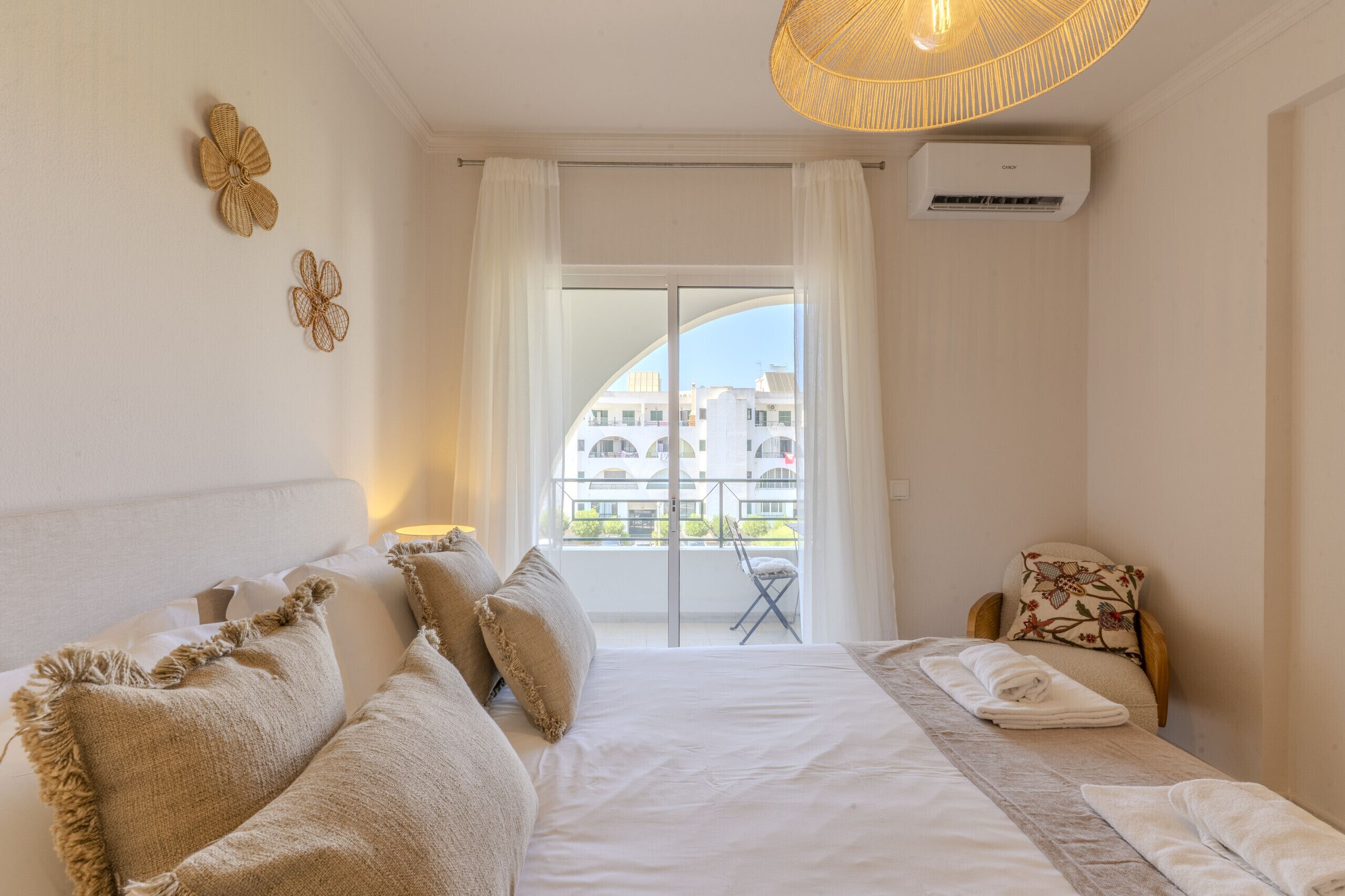 A hotel room with a bed, a chair, a balcony with a view, and an air conditioning unit.