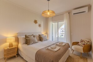 Habitación de hotel con cama, lámparas de noche, una silla, ventana con vista y aire acondicionado.