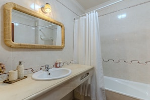 Un baño con un lavabo blanco, un espejo con marco de mimbre, una cortina de ducha y una bañera.