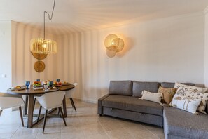 A modern living room with a dining area, featuring a grey sofa, a round dining table, and a hanging light fixture. - #413 Charming 1-Bedroom Apartment | Salgados, Albufeira (Albufeira)