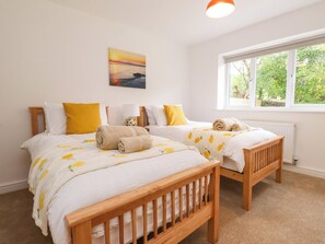 A bedroom with two wooden beds, a window with a view of greenery, and a painting on the wall. - 95 Cae America (Llanfairfechan)