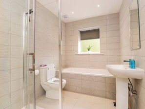 A bathroom with a glass shower enclosure, a toilet, a bathtub, and a sink with a mirror above it. - 95 Cae America (Llanfairfechan)