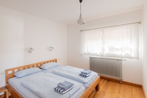 En dobbeltseng med træstel, to sengeborde med lamper, et vindue med let gardin og en radiator.