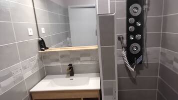 A small bathroom with a white sink, a mirror, a shower with a control panel, and tiled walls.