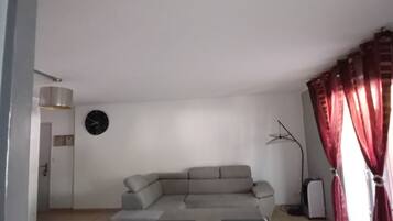 A living room with a sofa, a flat-screen TV, and a window with curtains.