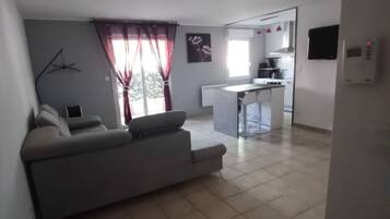 A living room with a sofa, a dining area with a table and chairs, and a kitchen in the background.