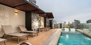 Un espace piscine aménagé sur le toit, avec des chaises longues et une vue sur le panorama urbain.