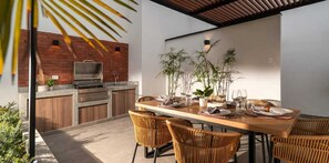 Un espace extérieur aménagé pour les repas, avec un mur en briques, un barbecue et une table dressée pour quatre personnes.