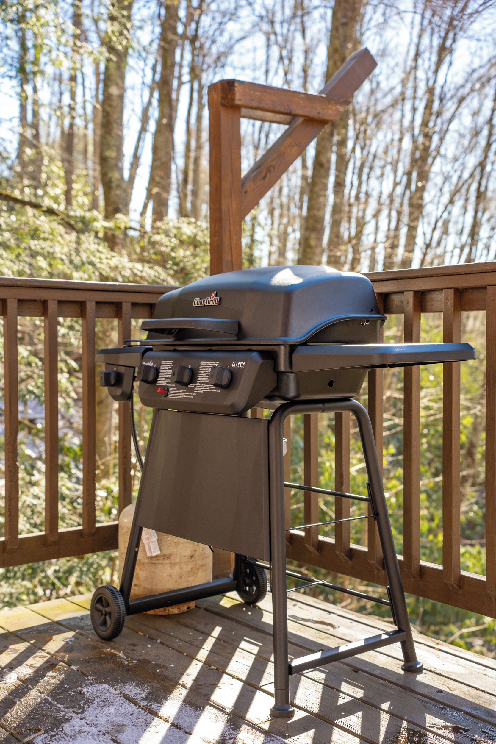 A portable charcoal grill on a wooden deck with a forest background.
