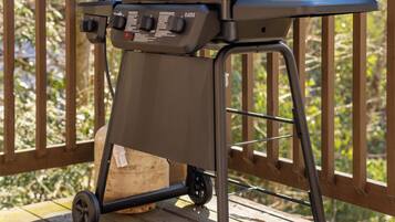 A portable charcoal grill on a wooden deck with a forest background.
