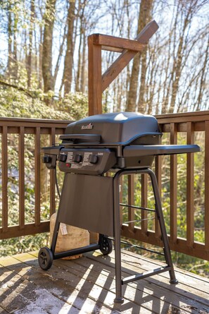 A portable charcoal grill on a wooden deck with a forest background.
