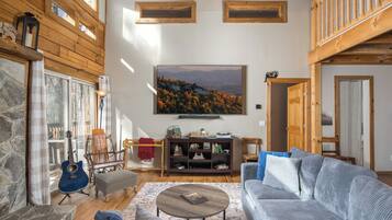 A cozy living room with a stone fireplace, a blue guitar, a large painting, and a wooden ceiling.