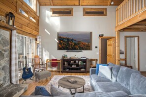 A cozy living room with a stone fireplace, a blue guitar, a large painting, and a wooden ceiling.