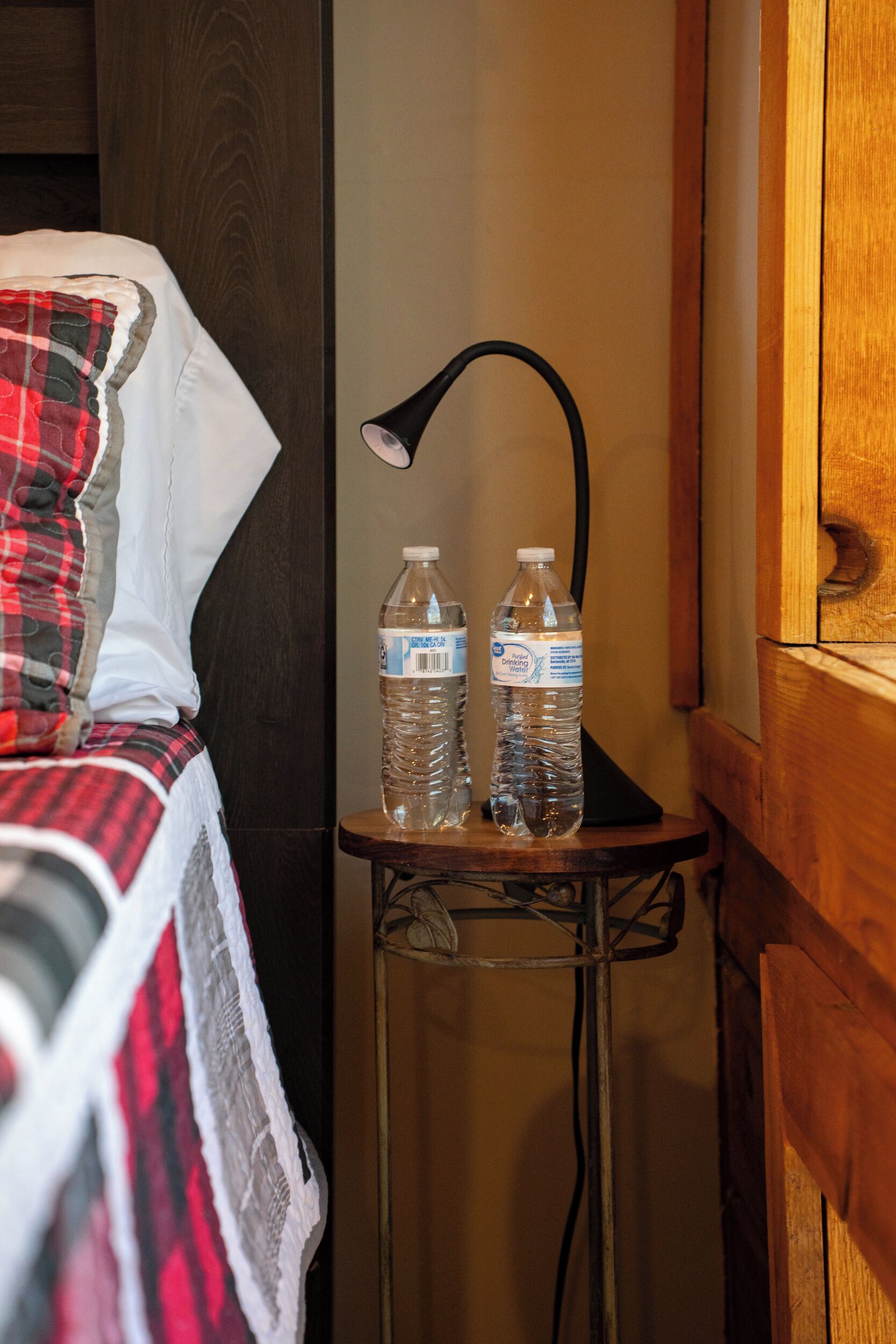 A bed with a plaid blanket, a bedside lamp, and two water bottles on a small table.