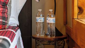 A bed with a plaid blanket, a bedside lamp, and two water bottles on a small table.