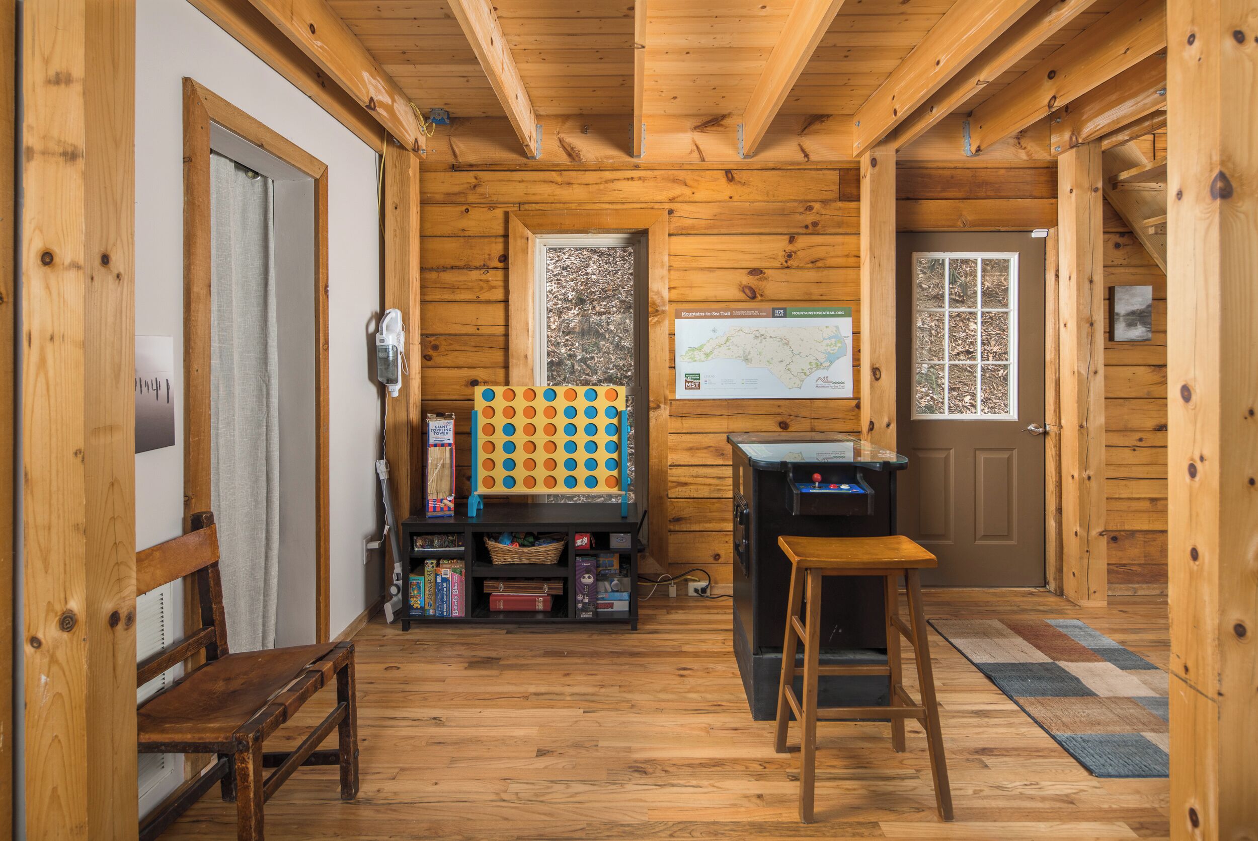 A wooden cabin interior with a wooden bench, a table, a map on the wall, and a small shelf with books and a basket.