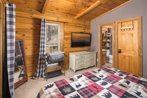 Una stanza con rivestimento in legno, un letto, una cassettiera, una televisione e un'anta che dà su un bagno.