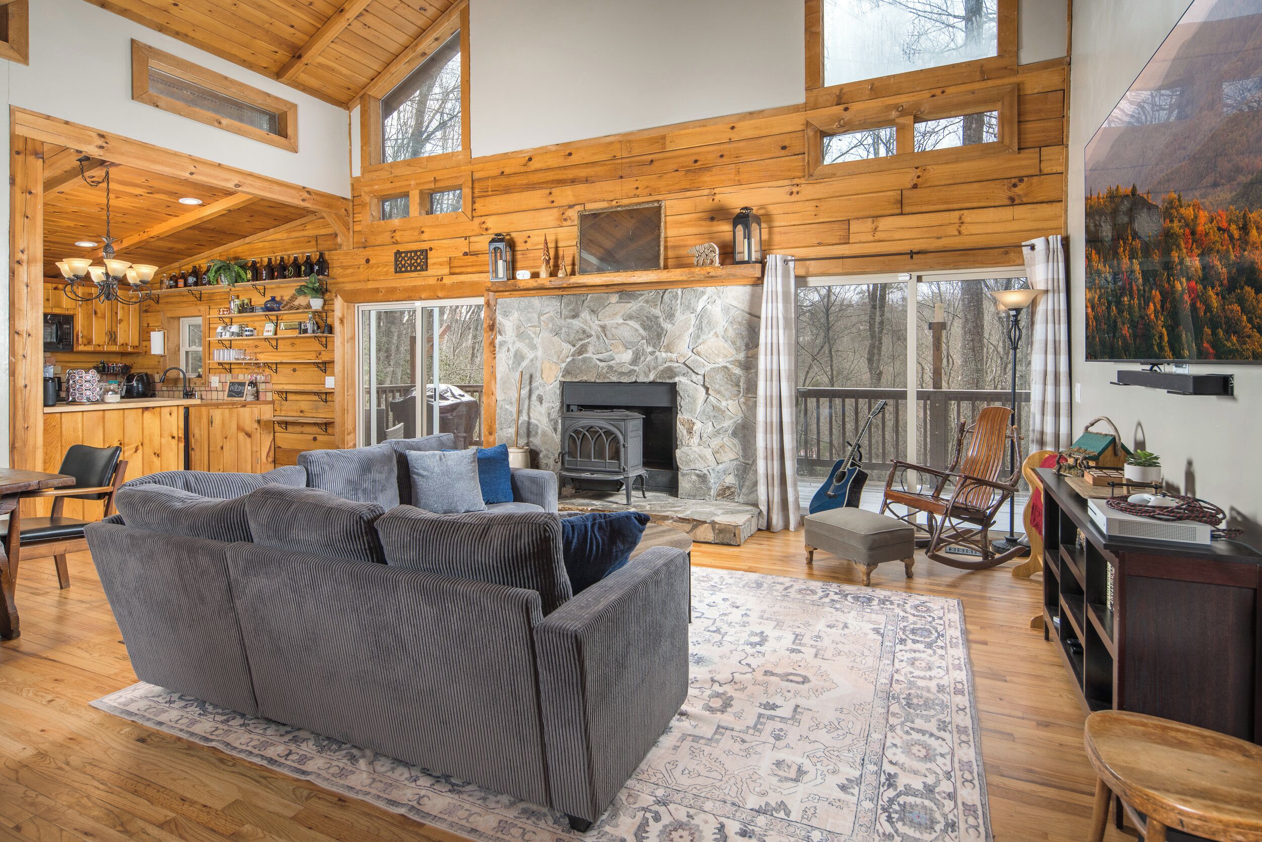 A spacious living room with a fireplace, wooden ceiling, and a large window.